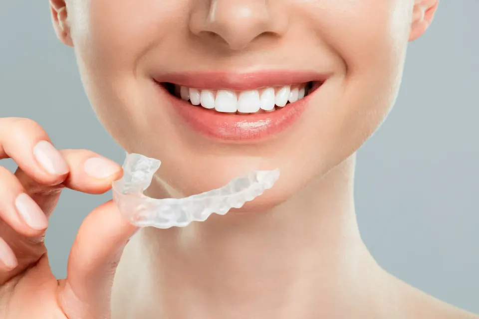 Patient holding Invisalign aligner trays next to a model of traditional metal braces at a dental office